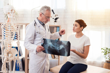 Doctor with stethoscope and female patient in office. Doctor is showing x-ray of hips.