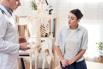 Doctor with stethoscope and female patient in office. Doctor is showing skeleton's hand.