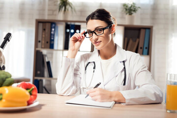 Female doctor sitting at desk in office with clipboard and stethoscope.