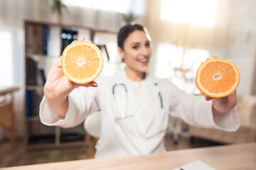 Female doctor sitting at desk in office with microscope and stethoscope. Woman is holding oranges.