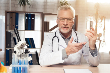 Doctor sitting at desk in office with microscope and stethoscope. Man is holding water.