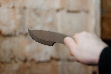 hand with metal knife, wooden block stand as target in background, throwing knives, sports competition, selective focus