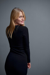 Smiling Woman in Black Dress Posing Against Neutral Background..