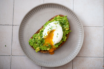 Smashed avocado sandwich with boiled poached egg with flowing yolk.