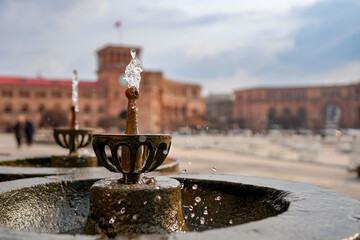 Pulpulak drinking fountains in the foreground with Republic Square and Government House in Yerevan, Armenia. Historic architecture with a clock tower, Armenian flag. Urban landmark and travel concept. © Alina Mosinyan