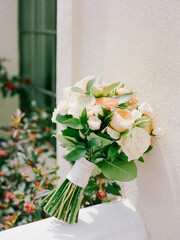 Beautiful floral bouquet resting against a white wall with greenery in a bright, sunny outdoor setting