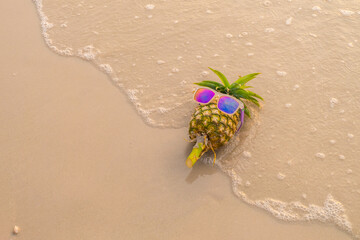Pineapple wearing sunglasses lying on the sand.