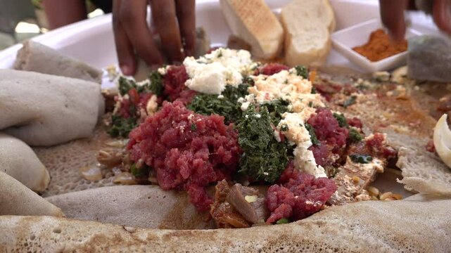 Ethiopian men eat fresh injera with raw meat, cheese and vegetables in restaurant, food and culture in Africa
