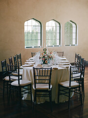 Elegant dining setup with floral arrangement in a well-lit venue featuring arched windows