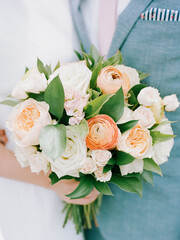 Elegant bridal bouquet featuring pastel flowers and green foliage held by a couple at a wedding ceremony