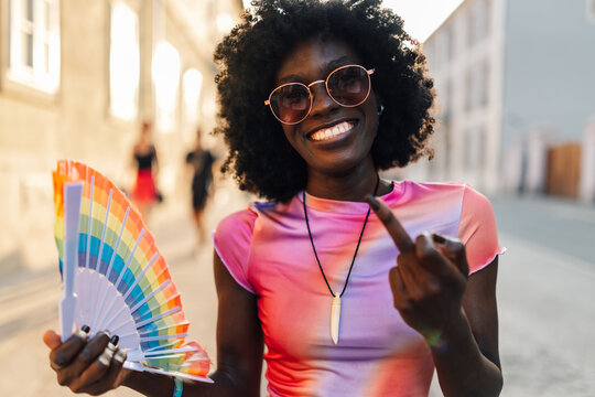 Young woman showing middle finger and holding rainbow fan during pride parade