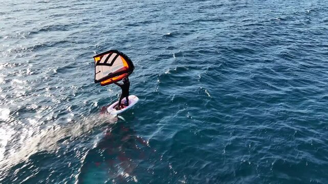 Aerial drone cinematic video of fit athlete practise hydro foil wing surfing in tropical exotic bay with emerald sea