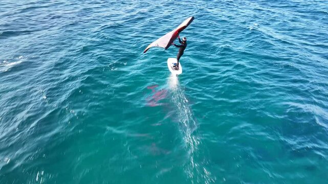 Aerial drone cinematic video of fit athlete practise hydro foil wing surfing in tropical exotic bay with emerald sea
