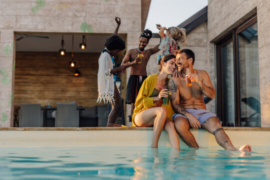 Happy couple enjoying drinks at poolside party with friends