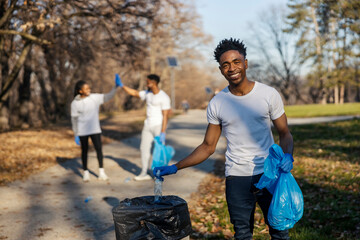 Eco conscious interracial activist putting plastic bottle into garbage bin and his two ecology team...
