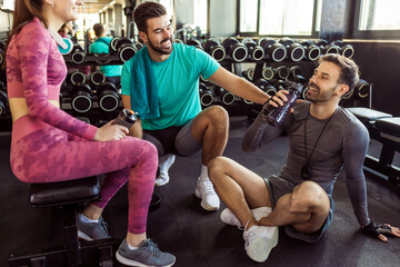 Three people rest at the gym. They talk, drink water and rest between training.