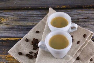 Two cups of espresso and roasted coffee beans on a wooden table.
