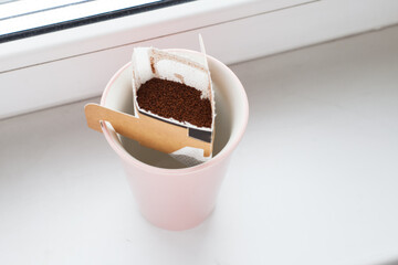 Drip bag in a ceramic cup on windowsill. Instant freshly brewed alternative filter drink in mug. Easy brew black coffee method for home, travel or office. cozy trendy lifestyle