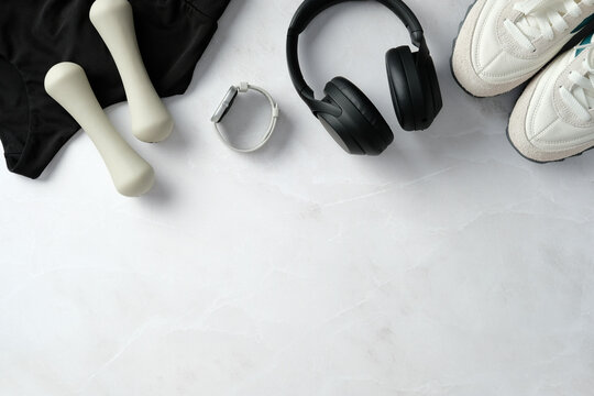 Flat lay fitness items: black sportswear, dumbbells, smartwatch, black wireless headphones, and sneakers on a marble background. Ideal for workout, fitness, and active lifestyle themes