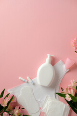 Feminine hygiene products on a pink background, including tampons, sanitary pads, menstrual cup, and a bottle of liquid soap, surrounded by flowers.