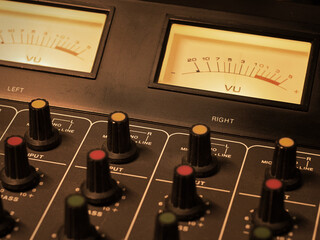 Detail of an analog studio mixer. Professional audio console with illuminated VU meters and knobs. Ideal for sound engineering, music production, or live radio show broadcasting and podcasts