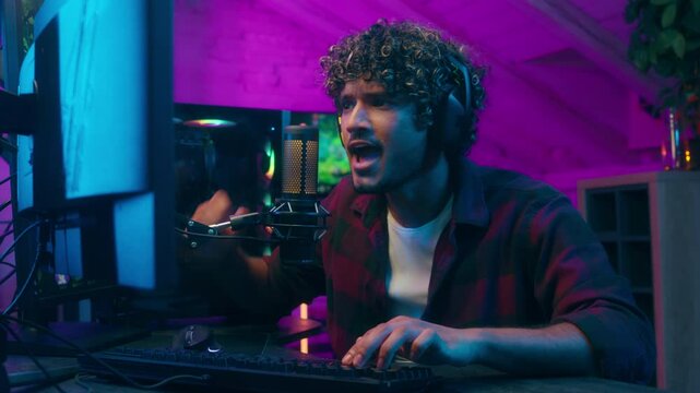 Excited Arabian Latino Muslim man playing computer gaming play gamer male guy streamer addict vlogger tournament cyber sport game discussing talk microphone blog influencer home neon online emotions