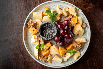 A visually appealing cheese platter featuring various cheese types, fresh grapes, and a small bowl...