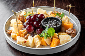 A visually appealing cheese platter featuring various cheese types, fresh grapes, and a small bowl of dark dip, garnished with mint leaves for added freshness.