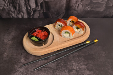 Set of sushi roll with rice and fish, wasabi and ginger on wooden serving board. Black chopsticks. Dark texture background with copy space. Japan menu. Asian food