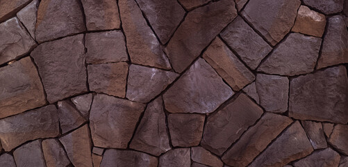 rough natural stone wall with irregular dark brown and gray stones. Textured surface with cracks and organic patterns