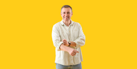 Mature man rolling up his sleeve on yellow background