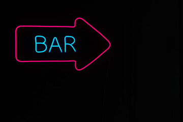 A neon sign with the words bar and a pink arrow on a black background.A glowing sign on a night street.Outdoor advertising.