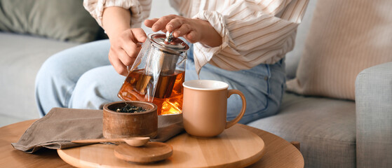 Young woman pouring hot tea into cup at home, closeup