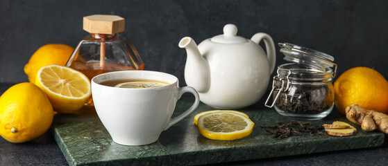 Board with cup of black tea, lemons and teapot on dark background