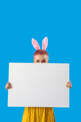 Obraz premium Young woman with bunny ears and blank poster on blue background. Easter celebration