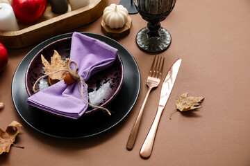 Stylish table setting with candle and autumn decor on brown background