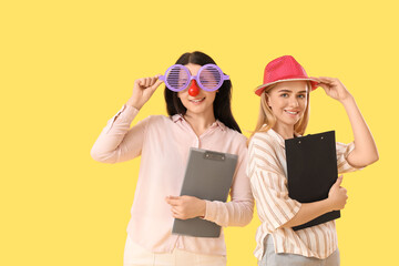 Business women in funny disguise with clipboards on yellow background. April Fools' Day celebration