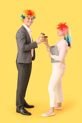 Business people in funny wigs with coffee cups on yellow background. April Fools' Day celebration