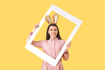Beautiful young woman in bunny ears with frame on yellow background. Easter celebration