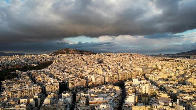 4k high resolution Athens aerial footage going downwards, flying over Eksarhia, Neapoli and Alexandras Avenue below big, dark clouds during golden hour.  