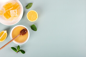 Acacia honey, honeycomb, lemon and mint leaves on blue background. Top view. Copy space.
