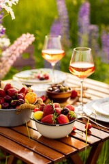 Romantic surprise, marriage proposal. Elegant decoration. Private wedding party for two, table set with floral decor, chandelier, fruits, wine in field or meadow. Summer, sunset, golden hour