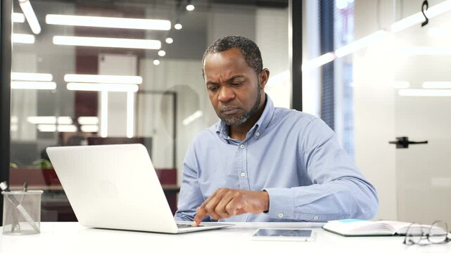 Worried african american businessman having problems with software or service on laptop computer sitting at workplace in office. Frustrated disappointed man complains about bad internet connection
