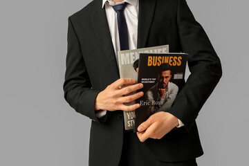 Young businessman with magazines on grey background