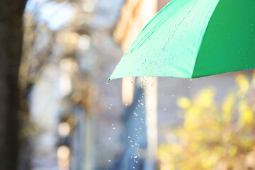 Open green umbrella under pouring rain outdoors, closeup. Space for text