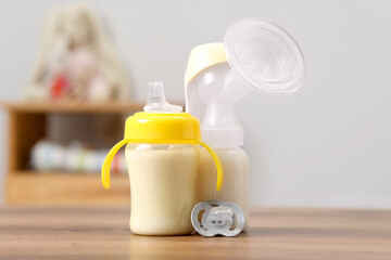 Feeding bottles with milk, breast pump and pacifier on wooden table indoors