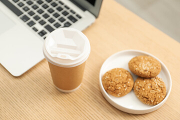 Paper cup, plate with cookies and laptop on wooden table, closeup. Mockup for design