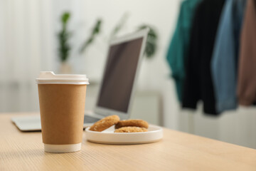 Paper cup, plate with cookies and laptop on wooden table indoors, closeup. Mockup for design