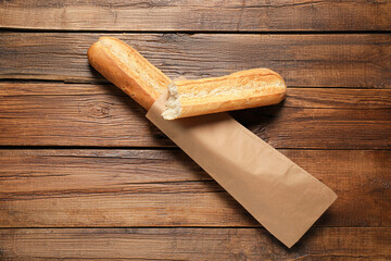 Paper bag with fresh baguettes on wooden table, top view