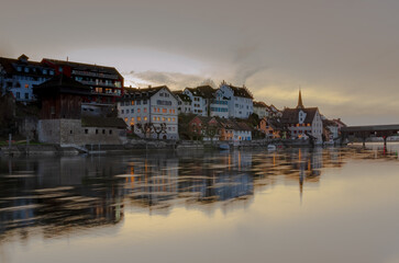 Naklejka premium Reflections of historic buildings along the calm river at sunset in a tranquil town